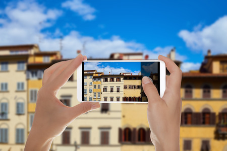 A man is making a photo of facades of different old houses on Piazza de Pitti in Florence, Italy on a mobile phoneの写真素材