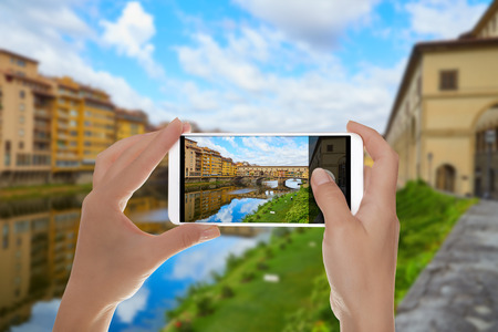 A man is making a photo of Ponte Vecchio Bridge in a summer sunny day without people on a mobile phoneの写真素材
