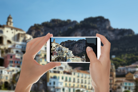 A tourist is taking a photo of the resort town of Amalfi in a clear summer sunny day on a mobile phoneの写真素材