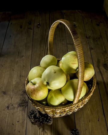 apples are in a wicker basket on the background of wooden boardsの写真素材