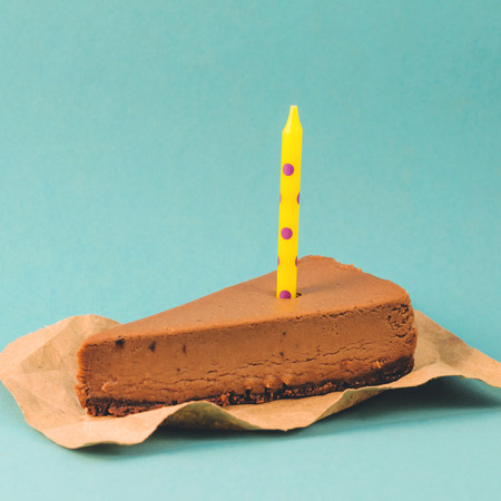 A piece of Chocolate cheesecake with a yellow candle on a blue background, close upの写真素材