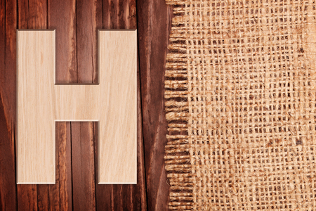Wooden alphabet letter symbol - H. On wooden table background with burlapの写真素材
