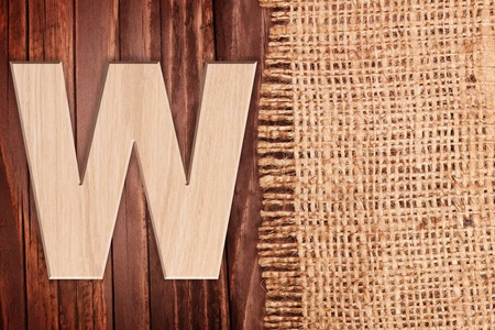 Wooden alphabet letter symbol - W.On wooden table background with burlapの写真素材