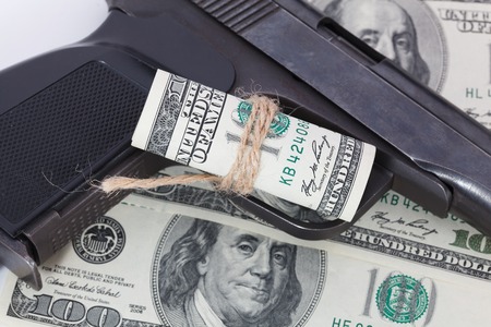 Black gun is lying on dollar bills