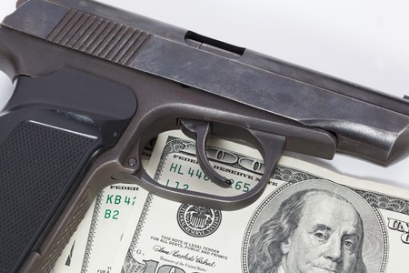 Black gun is lying on dollar bills