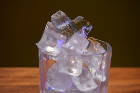 Ice cubes in a glass on a wooden table against a dark background
