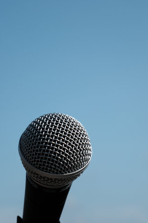 Close up of a microphone against a blue sky background with copy spaceの写真素材