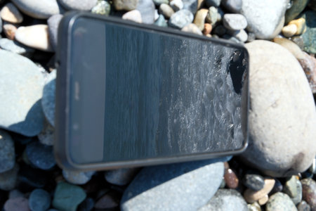 Mobile phone with blank screen on a pebble beach background.