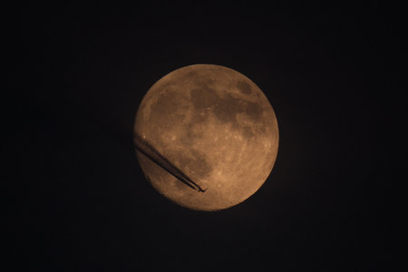 Airplane flying against the background of the moon. Contrail. The moon in the night sky.