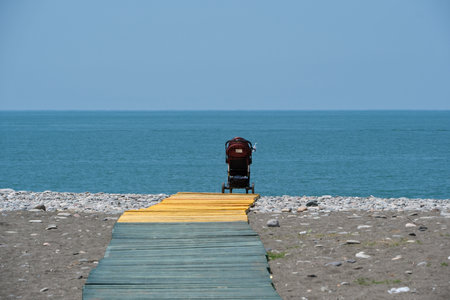 A single baby stroller on the beach of the Black Sea, Georgia. Wooden walkway to the beach with a stroller on itの写真素材