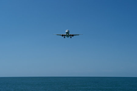 Airplane flying in the blue sky above the sea on sunny dayの写真素材