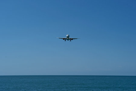 Airplane flying in the blue sky above the sea and the beachの写真素材