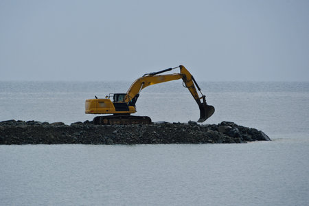 excavator working on the seashore in a cloudy dayの写真素材