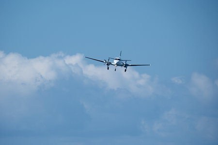 Twin-engine plane in the sky against the clouds. A propeller plane approaches the runway against a...