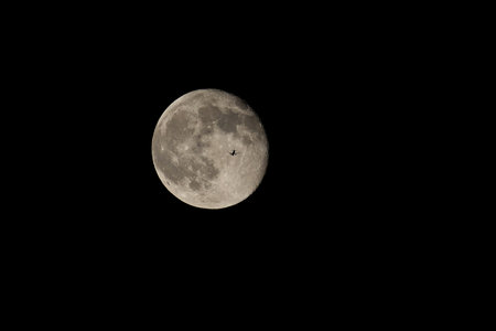 The silhouette of an airplane against the moon. Receding plane against the full moon in the dark night sky.の写真素材
