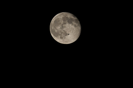 The silhouette of an airplane against the moon. Receding plane against the full moon in the dark night sky.の写真素材