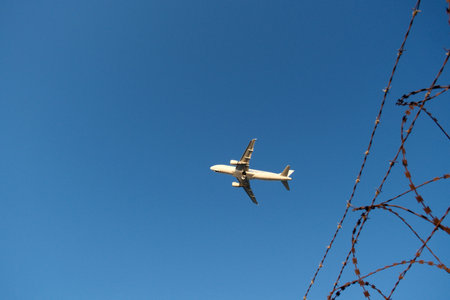 Airplane in the blue sky with barbed wire in the foreground