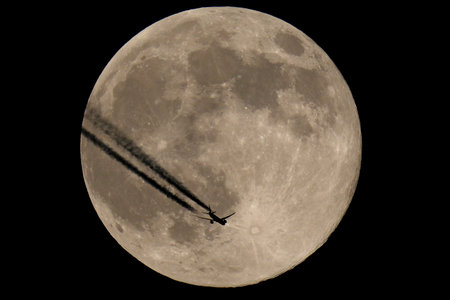 Plane flying over the moon in the night, closeup of photo