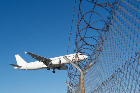 Plane over barbed-wire airport fence.の写真素材