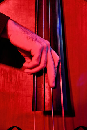 Close-up of double bass with hand against red backgroundの写真素材