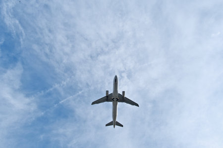 Airplane flying in the blue sky with white clouds on a sunny day. White Plane Overhead in Light Clouds. White Jet Soaring Overhead in Clear Blue Sky with Light Cloudsの写真素材
