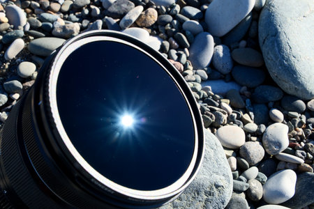 Camera Lens on Pebble Beach with Sun Reflection and Raysの写真素材