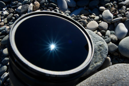 Camera Lens on Pebble Beach with Sun Reflection and Raysの写真素材