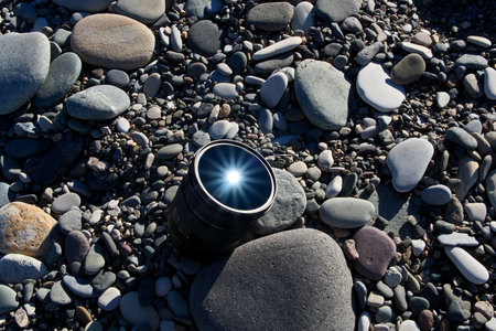 Camera Lens on Pebble Beach with Sun Reflection and Raysの写真素材