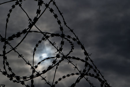 Barbed wire against the sky with clouds and sun in the background