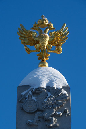 The Russian double-headed eagle atop an obelisk in Moscow's Alexander Garden, with snow beneath it and a clear blue sky above.の写真素材