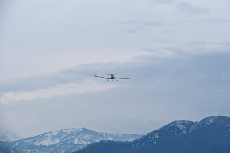 Light single-engine airplane climbing over snow-capped mountains in cloudy weather