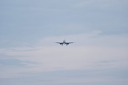 Airplane in the cloudy sky. White Passenger Plane Approaching Airport Runway Against Blue Cloudy Sky