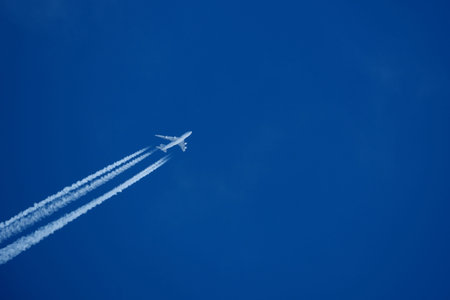 White airplane flying in the blue sky leaving a contrail with light clouds