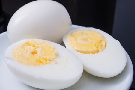 one boiled egg cut in half on a white plate and black backgroundの写真素材