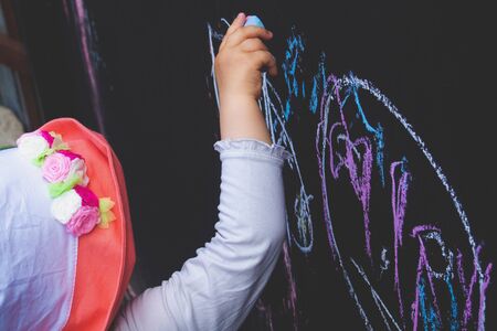 little girl child in a hat draws with chalk on a black fenceの写真素材