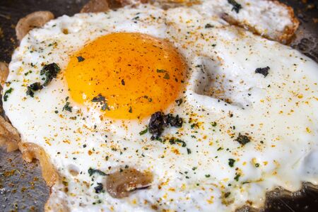 fried eggs in a steel pan with bacon and spicesの写真素材