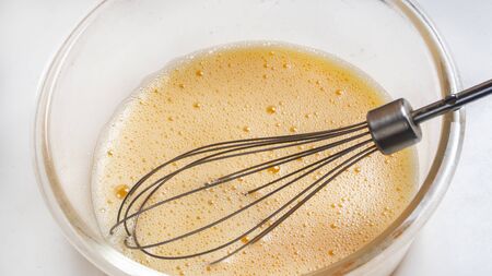 three beaten eggs for cooking French omelet in a glass bowl before whipping. Whisk for whipping lies...