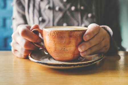 Woman's hand holding a beautiful brown ceramic cup of coffee. With a nude manicure.の写真素材