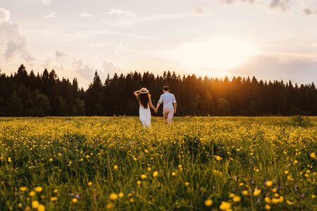 A couple in love runs across the field. Back view. Sunset light.の写真素材