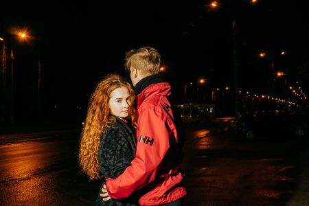 Loving couple in night sity. Beautiful red-haired girl and boy in red jacket.