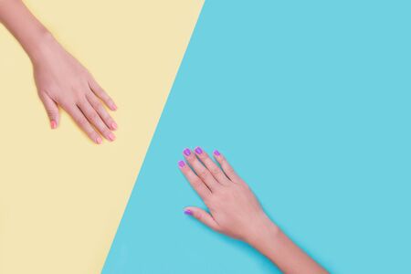 Bright trendy female manicure. Woman's hands with orange and violet manicure on yellow and blue background.の写真素材