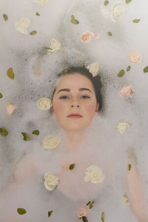 Young woman relax in foam bath with roses and leaves. Face close up.の写真素材