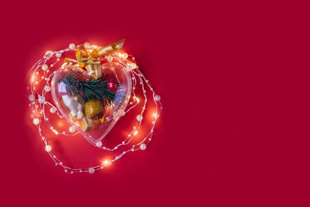Transparent heart with Christmas branch inside and a garland around on a red background. Copy space. Flat lay.の写真素材