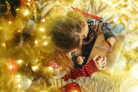 Mother and son open gift box near the lighting christmas tree. Christmas decoration. Golden bokeh.
