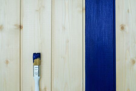 The board is painted blue and a brush with blue paint on a wooden background. Blue - color of the...