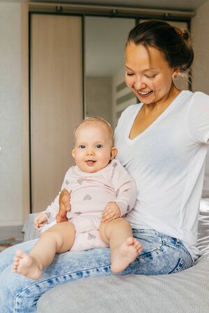 Happy young mother with cute baby girl. At home, light interior. Vertical.