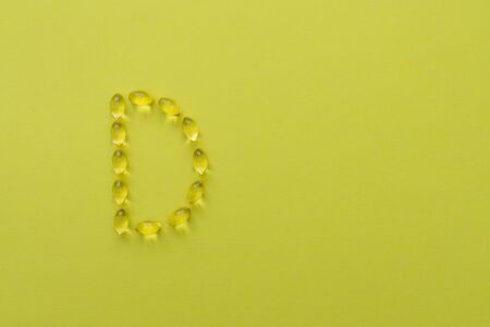 Vitamin d gel capsules on yellow background. Letter D. Copy space.