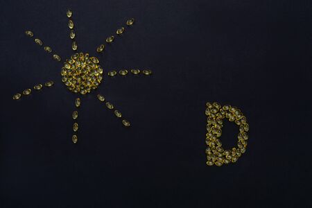 Vitamin d gel capsules on black background. As sun and letter D from capsules.