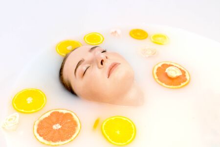Pretty girl in bath with milk and orange, lemon, grapefruit slices. Only face under water. Natural...