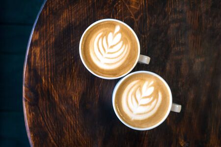 Two cups of cappuccino with latte art on brown wooden background. Perfect foam, top view, place for...
